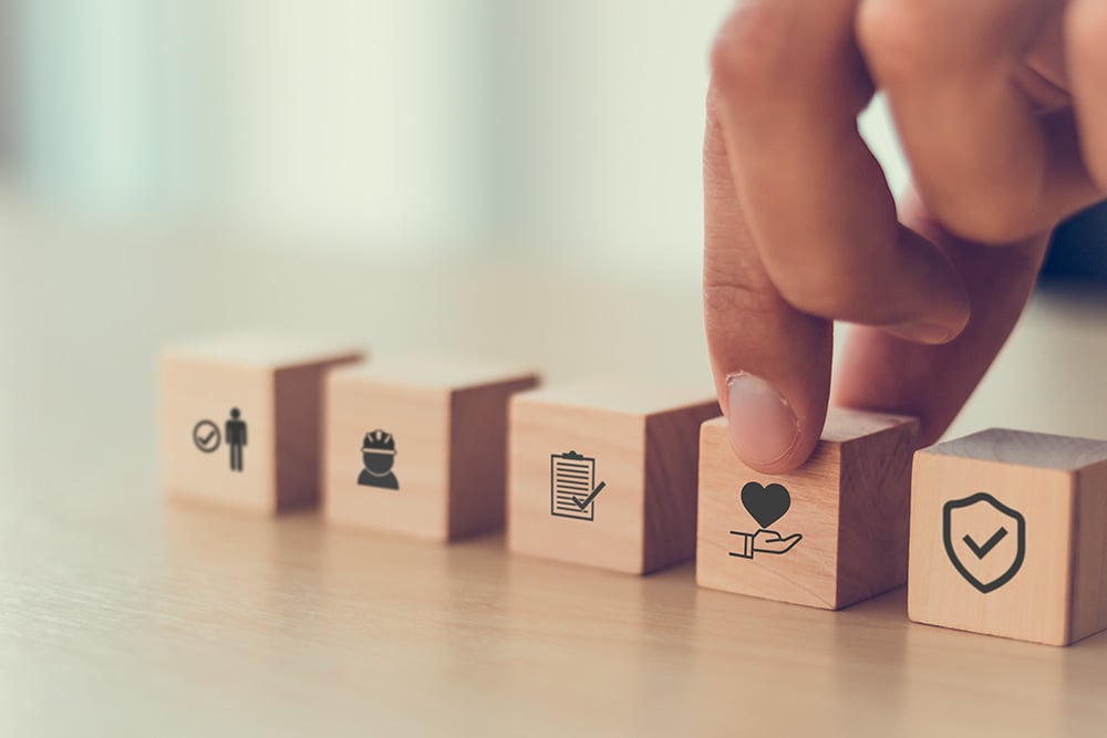 An arrangement of small blocks on a table, with illustrations on one side of each. A hand is gesturing towards one with a health related illustration.