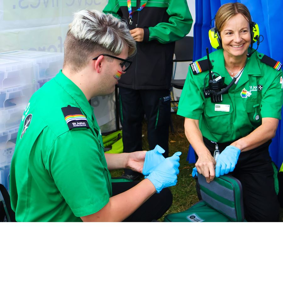 Two volunteers crouched in a first aid treatment tent putting on blue gloves.