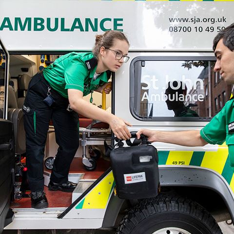 A volunteer standing in an ambulance passing a defibrillator to another volunteer.
