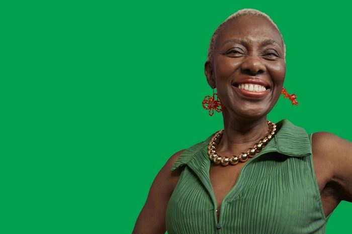 Woman wearing a green top and red earrings standing with her hands on her hips smiling, in front of a green background.