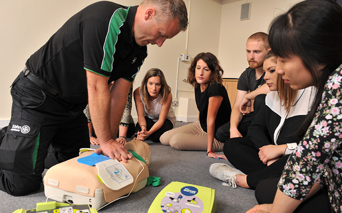 A group of first aid students observing a defibrillator demonstration.